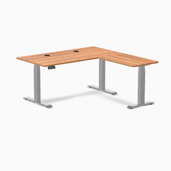 Desky L-Shape Laminate Sit Stand Desk in Prime Oak with gray frame and grommets.