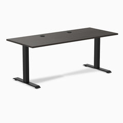 Desky Zero fixed-height office desk with burnished wood laminate top, two grommets, and matte black steel frame.
