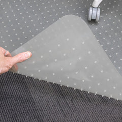 Hand lifting a corner of a translucent Desky Chair Mat with studded underside on gray carpet.
