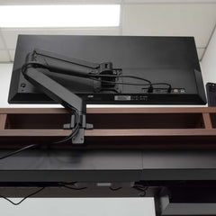 Black Desky Single Monitor Arm securely mounted to a dark wood desk, supporting a large black monitor.