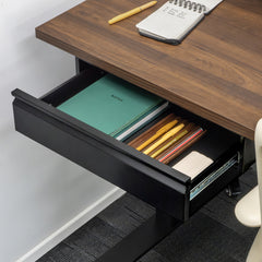 Black steel Desky Under Desk Drawer, open to reveal a green notebook and pens, mounted under a dark wood desk.