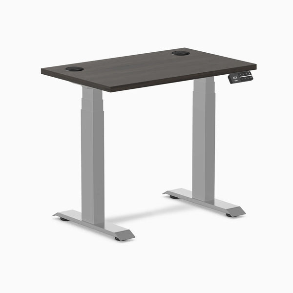 Desky Dual Mini sit-stand desk with burnished wood top, gray frame, and grommets.
