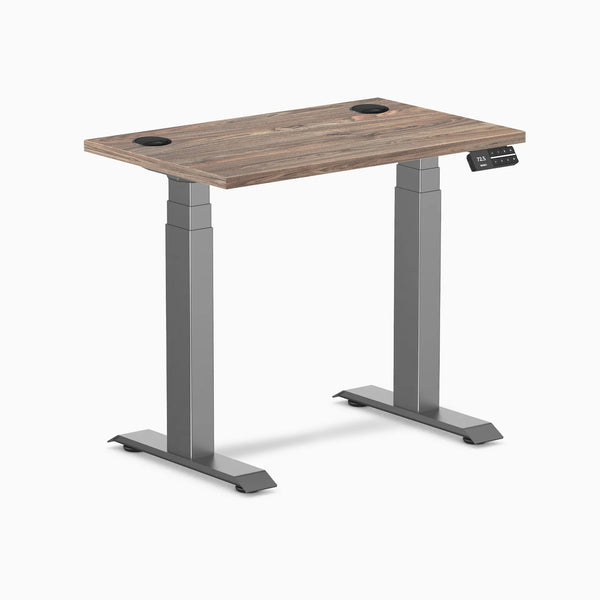 Desky Dual Mini sit-stand desk with natural walnut top, space gray frame, and grommets.