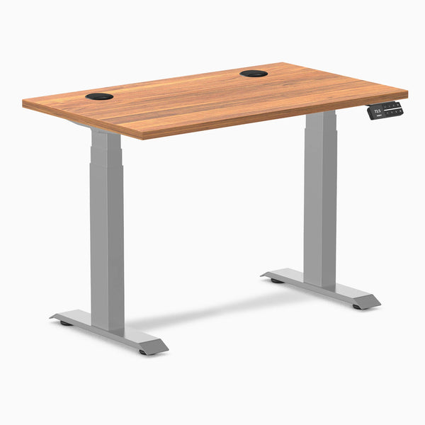 Desky Dual Mini sit-stand desk with Prime Oak top, gray frame, and two grommets.