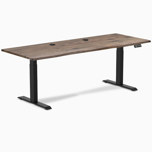 Desky Dual sit-stand desk with natural walnut laminate top, matte black frame, and two grommets.